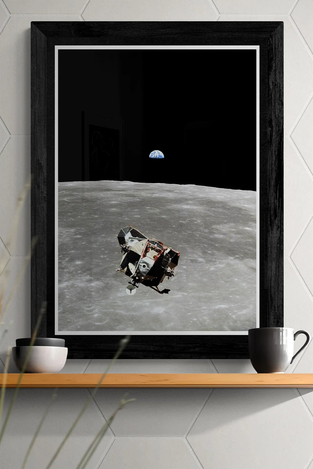 Apollo 11 Lunar Module poster with Earth in the distance, framed and displayed on a shelf with contemporary decor for space enthusiasts.