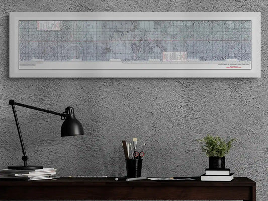 Apollo 10 Lunar Map | Apollo 10 Moon Map | Rocket Blueprint Posters | Home Office Poster | A dark wooden desk with a black lamp, a collection of pencils, and a small plant. The textured gray wall behind the desk features a white-framed Apollo target of opportunity flight chart, highlighting the moon's detailed surface.