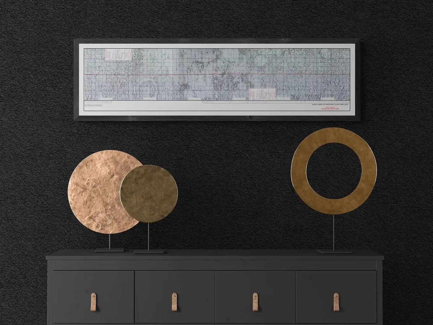 Apollo 10 Lunar Map | Apollo 10 Moon Map | Rocket Blueprint Posters | Bedroom Decor | A black dresser with bronze accents, adorned with two circular metal sculptures, one solid and one ring-shaped. The wall above the dresser showcases a white-framed Apollo target of opportunity flight chart against a dark background