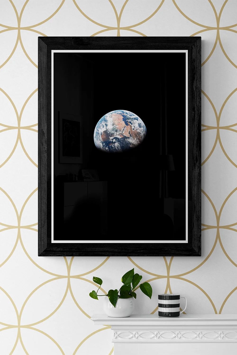 Framed poster of Earth as seen from space, showcasing a view over Africa, styled on a white mantel with a green plant and striped mug.