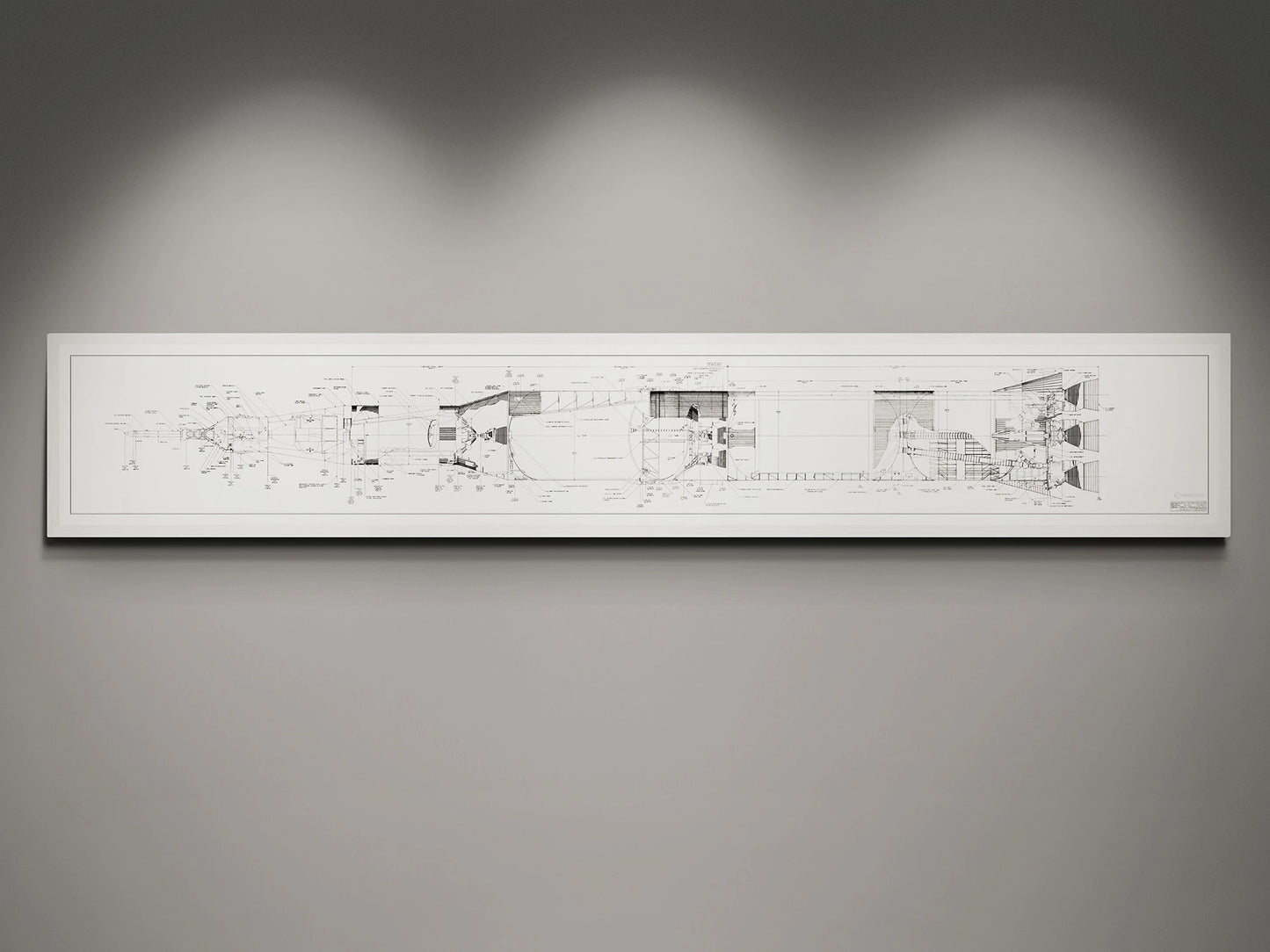Apollo Saturn V | Rocket Blueprint Posters | NASA | A white-framed detailed blueprint of the NASA Saturn V rocket, showcasing technical schematics in black on a white background. The blueprint is displayed on a gray wall, illuminated by soft overhead lights.