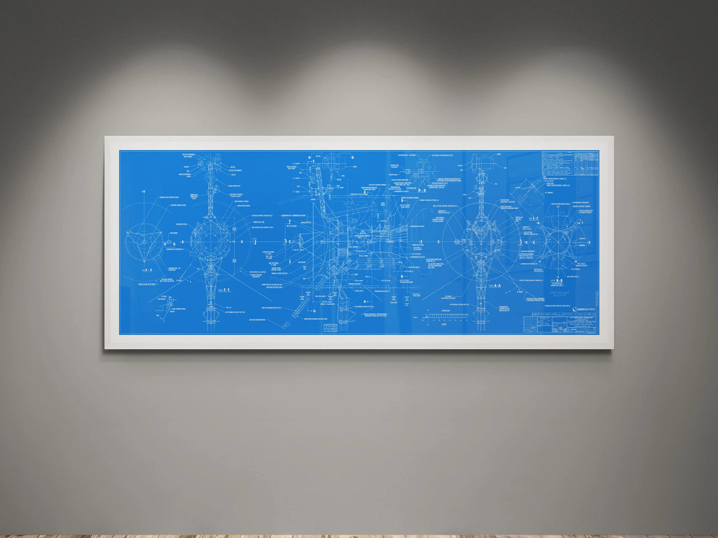 Voyager Space Probes Blueprint | Rocket Blueprint Posters | NASA | JPL | A white-framed blueprint of the NASA Voyager Probes is displayed on a gray wall. The blueprint features detailed schematics and annotations of the spacecraft components in a vibrant blue background. The framed artwork is illuminated by overhead lighting, highlighting the intricate design and technical details of the probes.