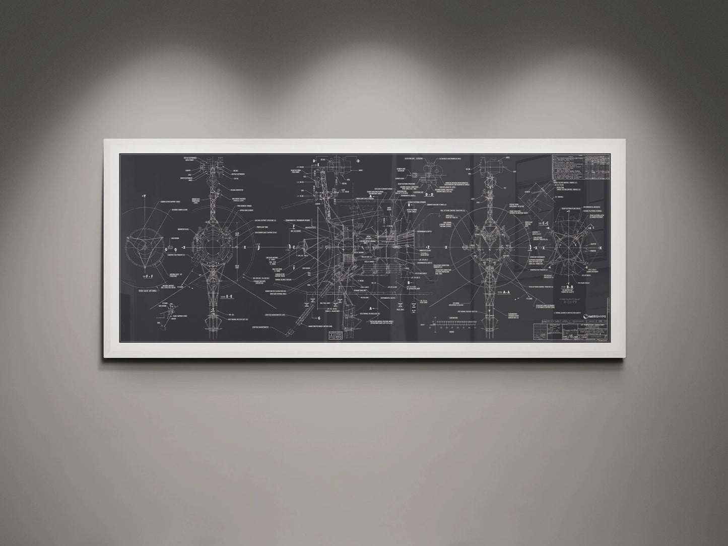 Voyager Space Probes Blueprint | Rocket Blueprint Posters | NASA | JPL | The framed blueprint of the NASA Voyager Probes, set against a gray wall, features a detailed and annotated design on a charcoal background. The white frame complements the technical artwork, while the overhead lighting highlights the precision and complexity of the spacecraft's schematics.