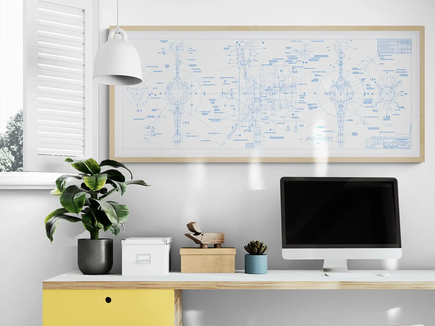 Voyager Space Probes Blueprint | Rocket Blueprint Posters | NASA | JPL | A minimalist desk setup featuring a yellow drawer, a black potted plant, a white storage box, and a wooden airplane model. Above the desk, a framed white blueprint of the Voyager Probes, detailed in blue, hangs on the wall. The scene is well-lit with natural light from a nearby window with white shutters.