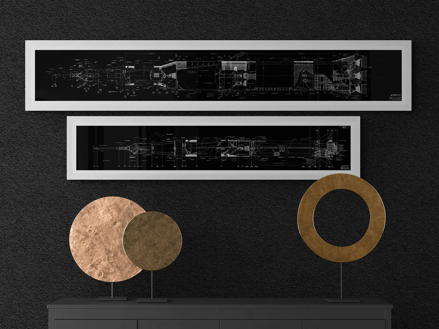 Apollo Saturn Blueprint | NASA posters | Two black-framed Apollo Saturn rocket blueprints, one larger and one smaller, are displayed on a dark wall. The detailed white schematics contrast with the black background. Below, a dark dresser with two circular metallic sculptures, one bronze and one gold, adds a touch of elegance.