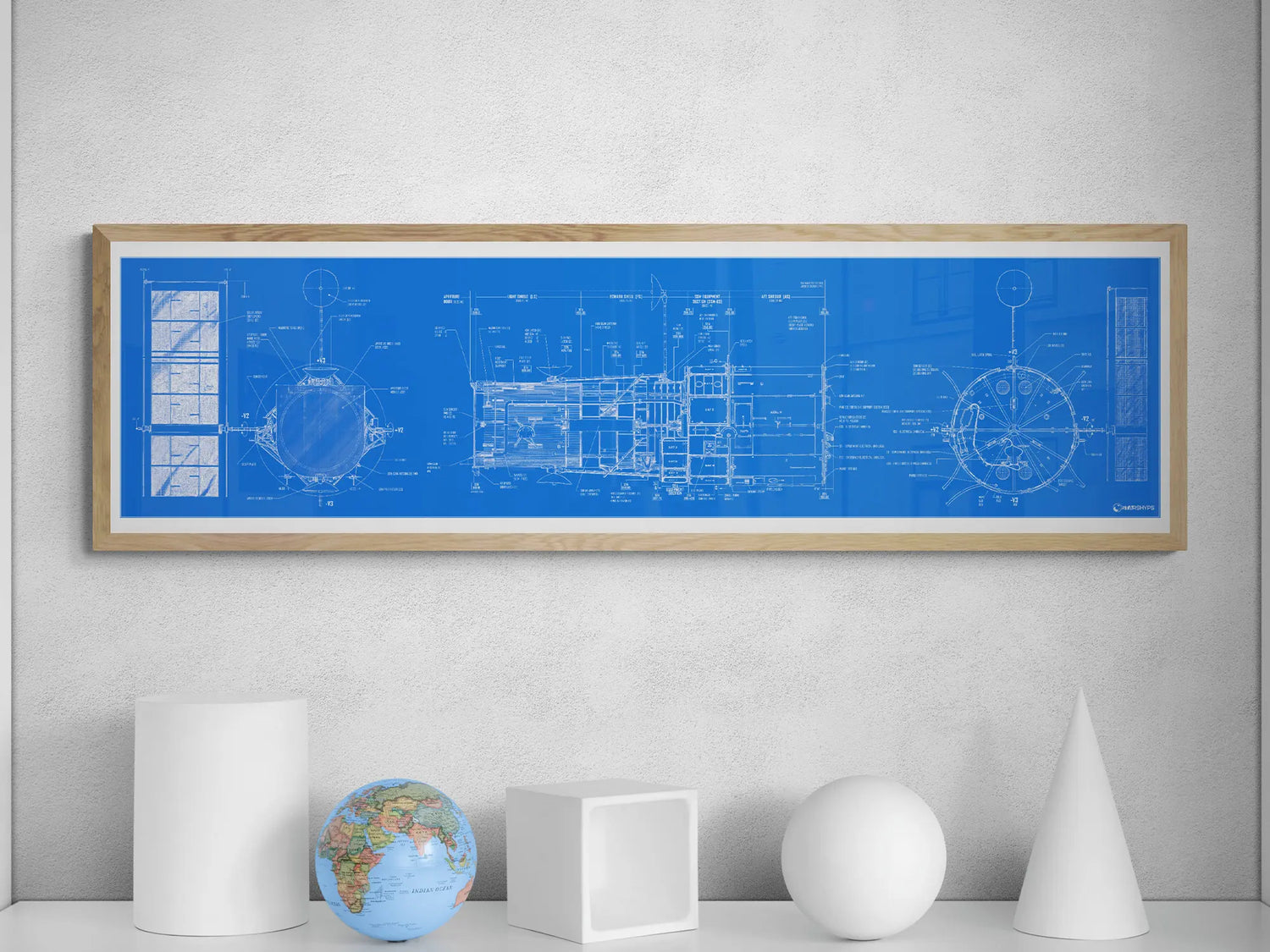 Hubble Space Telescope Blueprint | Rocket Blueprint Posters | A detailed blueprint of the Hubble Space Telescope is framed in light wood and hung on a white wall. The blueprint is blue with white schematic drawings and labels. Below the frame, a white shelf holds a simple collection of objects: a white cylinder, a globe, a white cube, and a white cone.