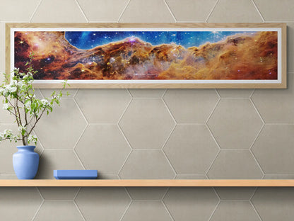 James Webb Space Telescope 'Cosmic Cliffs' framed panoramic poster displayed on a stylish wall with hexagonal tile patterns, complemented by minimalistic decor. Space-themed art print perfect for modern home or office decor.