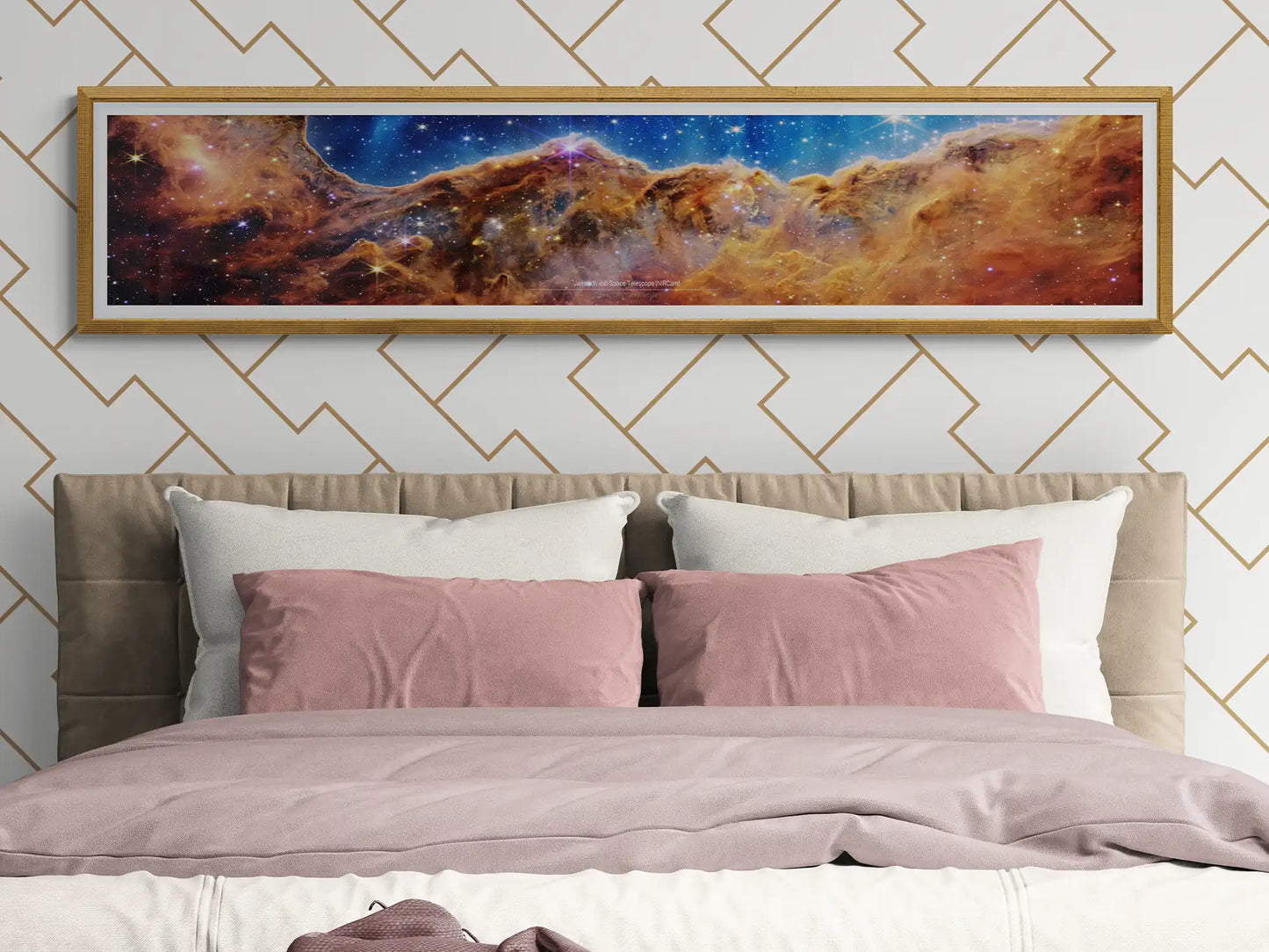 Framed James Webb Space Telescope 'Cosmic Cliffs' panoramic poster above a modern bedroom setting, featuring stylish geometric wallpaper and soft bedding. Space-themed wall art for sophisticated home décor and astronomy lovers.