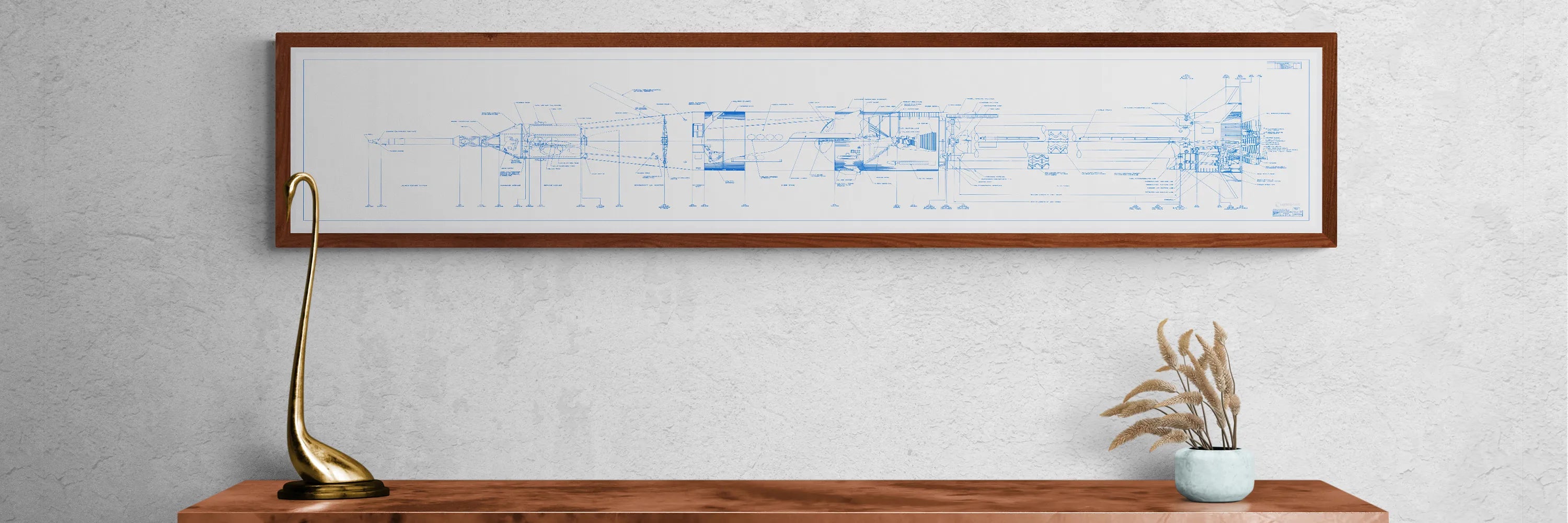 Apollo Saturn 1B Blueprint | NASA posters | Technical blueprint Diagram | A framed blueprint poster of the Saturn 1B rocket hangs on a light-colored wall above a wooden table. The detailed technical drawing is set against a white background with blue lines. On the table are a modern brass lamp with a curved design and a small potted plant with dried grass.