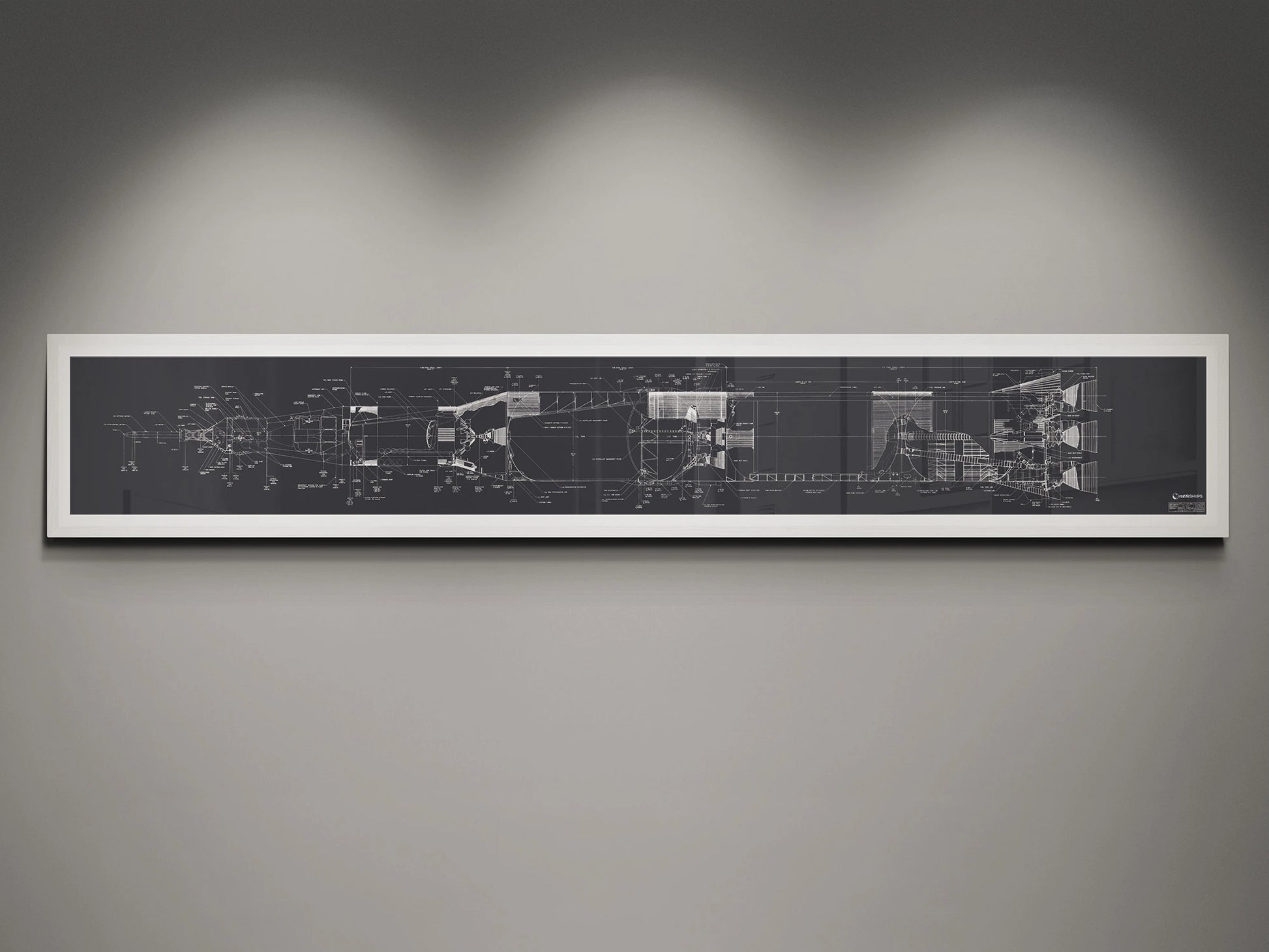 Apollo Saturn V | Rocket Blueprint Posters | NASA | A framed blueprint of the NASA Saturn V rocket, showcasing intricate technical drawings in white on a charcoal background. The blueprint is mounted on a gray wall and highlighted by soft overhead lights.