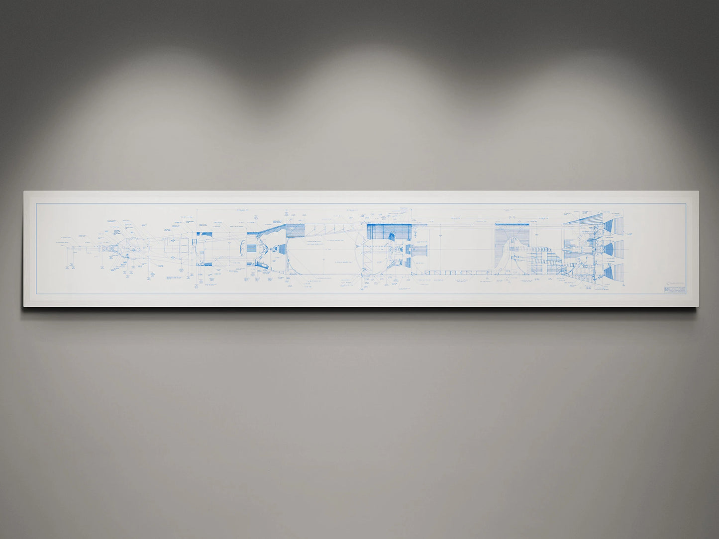 Apollo Saturn V | Rocket Blueprint Posters | NASA | A detailed blueprint of the NASA Saturn V rocket displayed in a white frame against a gray wall. The blueprint features blue technical schematics on a white background, illuminated by subtle overhead lighting.