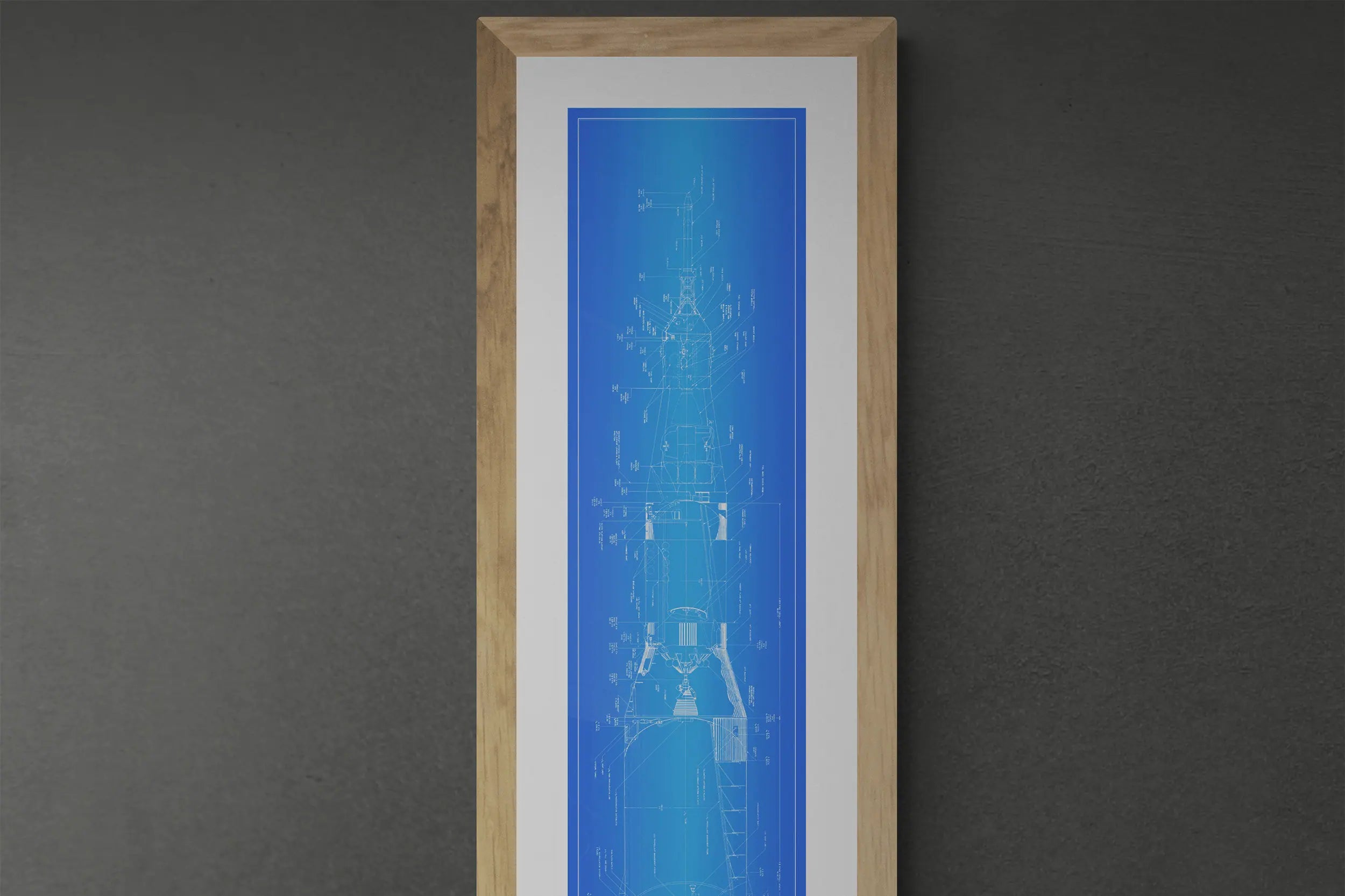 Rocket Posters | NASA | A vertical framed blueprint poster of the Saturn V rocket is displayed on a dark wall. The poster features detailed technical drawings in blue, enclosed in a wooden frame.