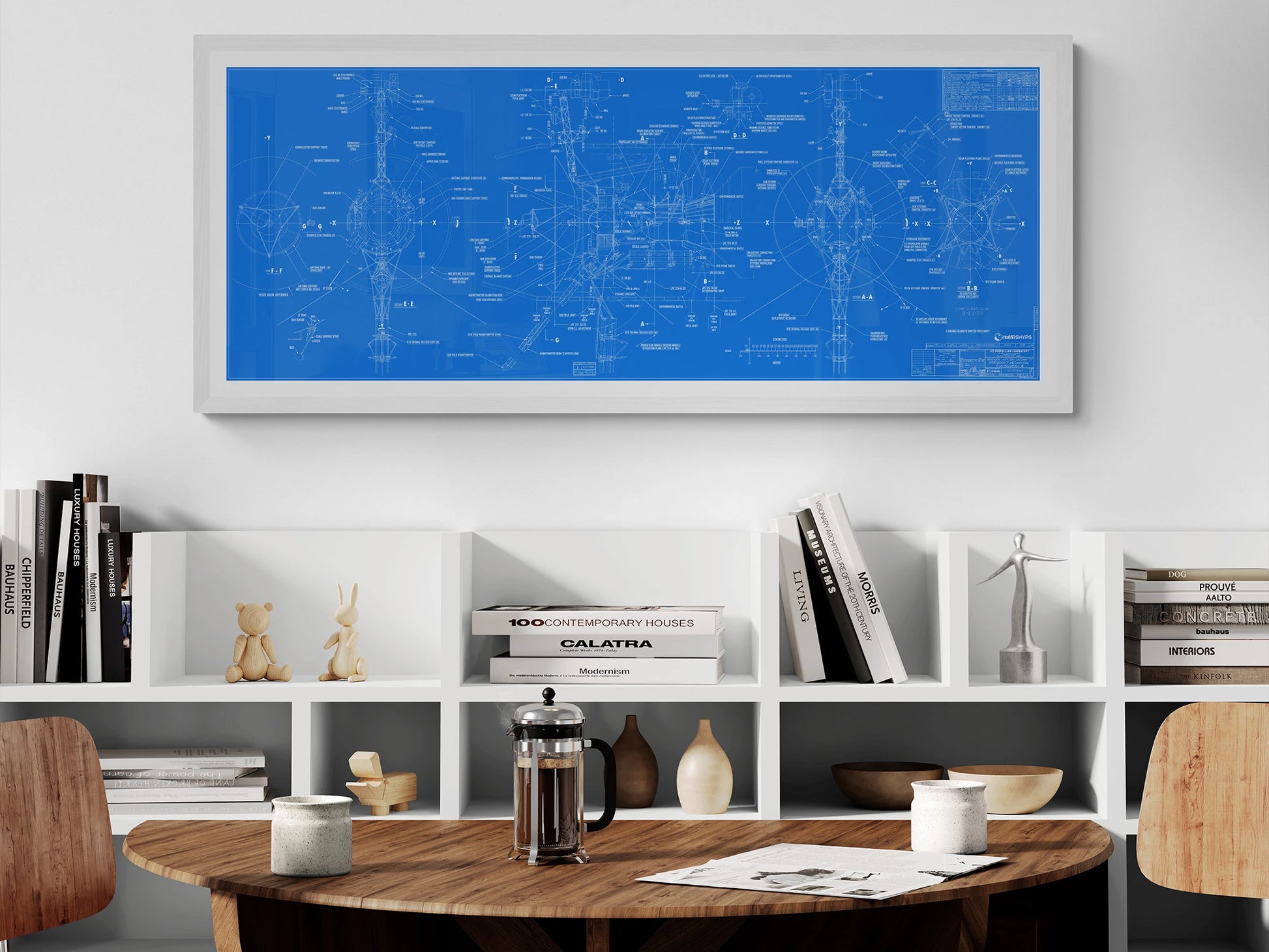 Voyager Space Probes Blueprint | Rocket Blueprint Posters | NASA | JPL | A cozy dining setup featuring a wooden table, coffee maker, and a white bookshelf. A large framed blue blueprint of the Voyager Probes, detailed with white technical sketches, is displayed above the bookshelf.